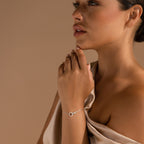 Woman in a beige dress wearing the Interlocking Opal Inlay Bracelet, featuring a circular opal charm, posing against a tan background—ideal for those who appreciate minimalist jewelry.