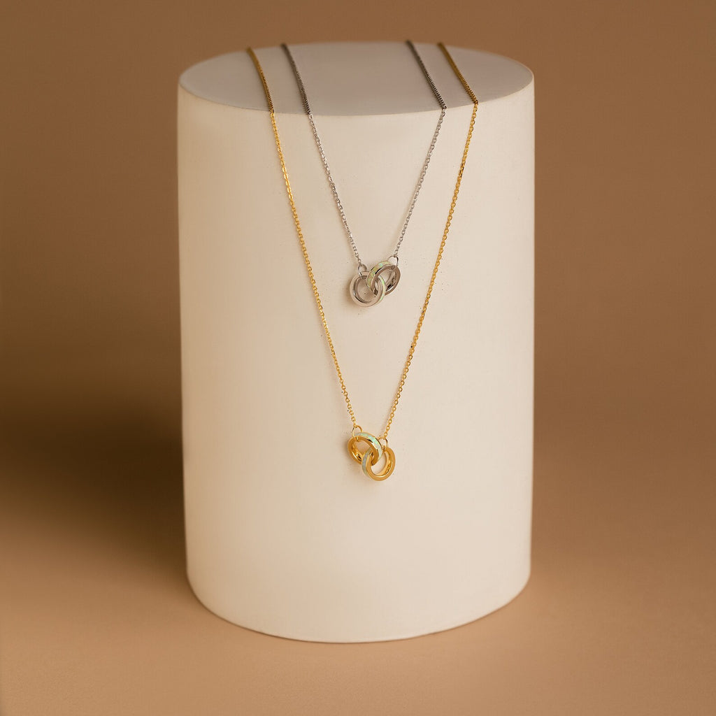 The Interlocking Opal Inlay Necklace features silver and gold pendants with opal inlays, elegantly displayed on a stand—a beautiful anniversary gift symbolizing infinite love.