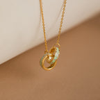 The Interlocking Opal Inlay Necklace, featuring gold chain and pale green opal-like rings symbolizing infinite love, is displayed on a beige background. A perfect anniversary gift.