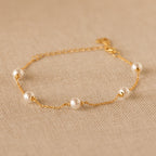The Pearl Station Bracelet features five evenly spaced pearls on a delicate gold chain, elegantly displayed on beige textured fabric—a timeless piece of modern jewelry.