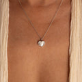 The Pearl Heart Locket Necklace, a nostalgic silver pendant, rests on the bare chest and is paired with a cream-colored garment.