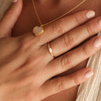 A hand with light pink polish wears the Marquise Opal Diamond Ring and a gold heart necklace on bare skin.
