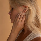 A woman with blonde hair touches her ear, highlighting a Marquise Opal Statement Ring and a sleeveless light top, radiating classic style.