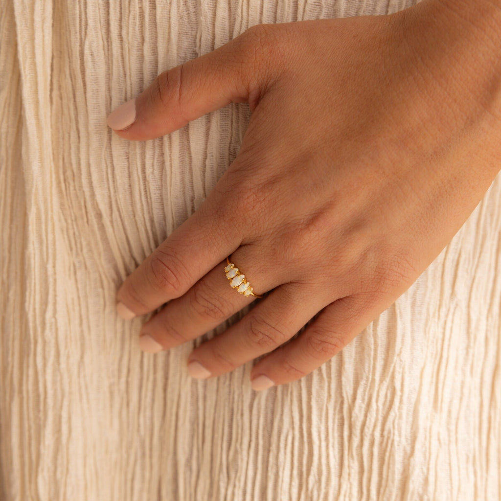 A hand adorned with the Marquise Opal Statement Ring rests on beige textured fabric, radiating vintage allure.