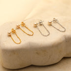 Two pairs of Pearl Chain Studs, one in gold and one in silver, are displayed on a beige stone surface.