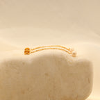 The Pearl Chain Studs feature delicate chains with small pearl drops, displayed on a smooth, light stone surface.