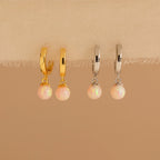 The Opal Drop Earrings Set features two pairs of hoop earrings—one gold and one silver—with opal dangles, perfect for layering your jewelry on a beige fabric display.