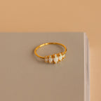 The Marquise Opal Statement Ring features five white opals, shown on a closed beige book against a soft beige background, radiating vintage allure and classic style.