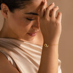 A woman with closed eyes touches her forehead, wearing a cream-colored top and the Interlocking Opal Inlay Bracelet, a piece that brings minimalist jewelry elegance to her look.