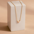 The Pink Opal Butterfly Necklace features a gold chain with a delicate pink opal butterfly pendant, beautifully displayed on a rectangular white block for an elegant touch.