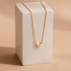 The Pink Opal Butterfly Necklace features a gold chain with a delicate pink opal butterfly pendant, beautifully displayed on a rectangular white block for an elegant touch.