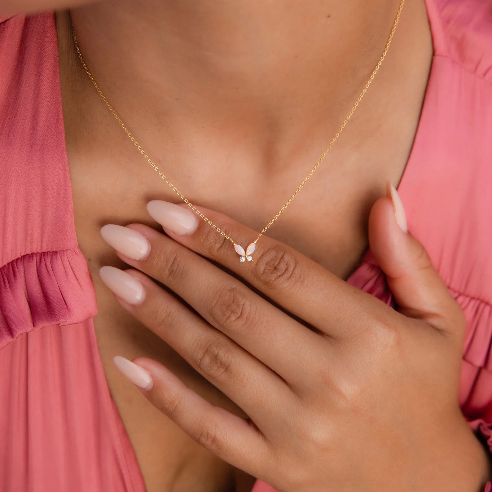 A person wearing the Opal Butterfly Necklace Set and a pink top touches their chest with manicured nails.