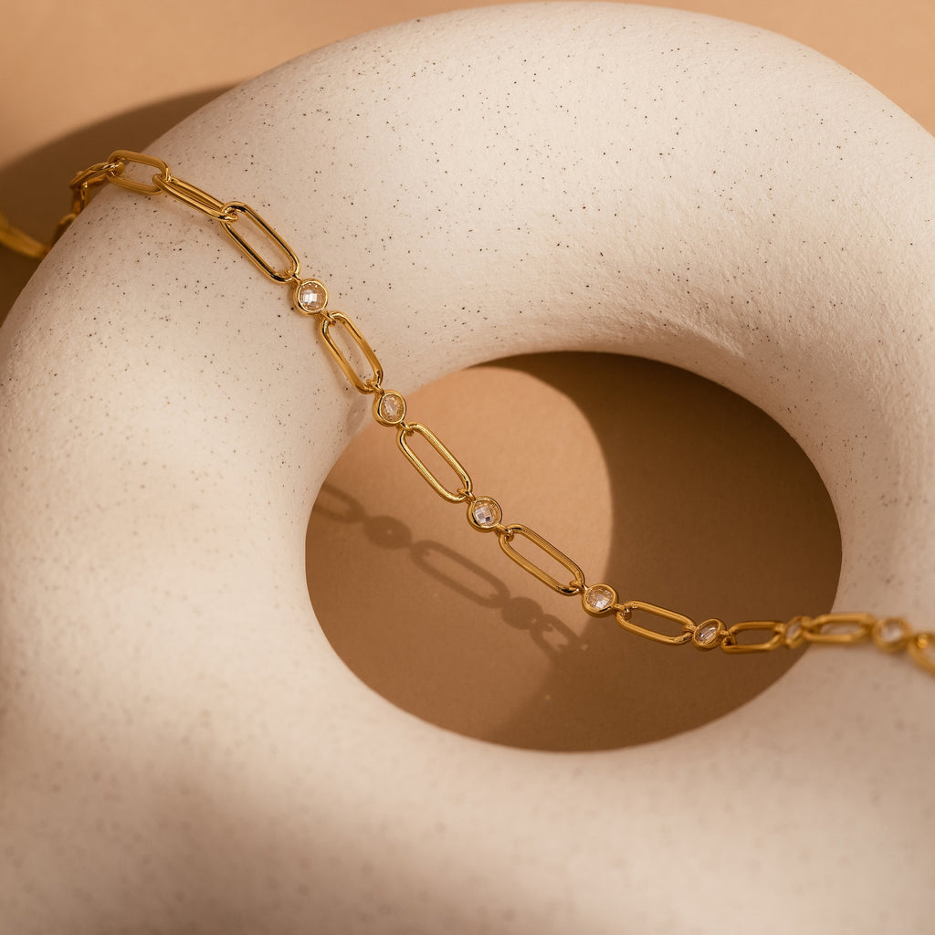 The Diamond Paperclip Necklace, adorned with clear gemstones, drapes elegantly over a smooth white, donut-shaped sculpture, showcasing the refined allure of statement jewelry.