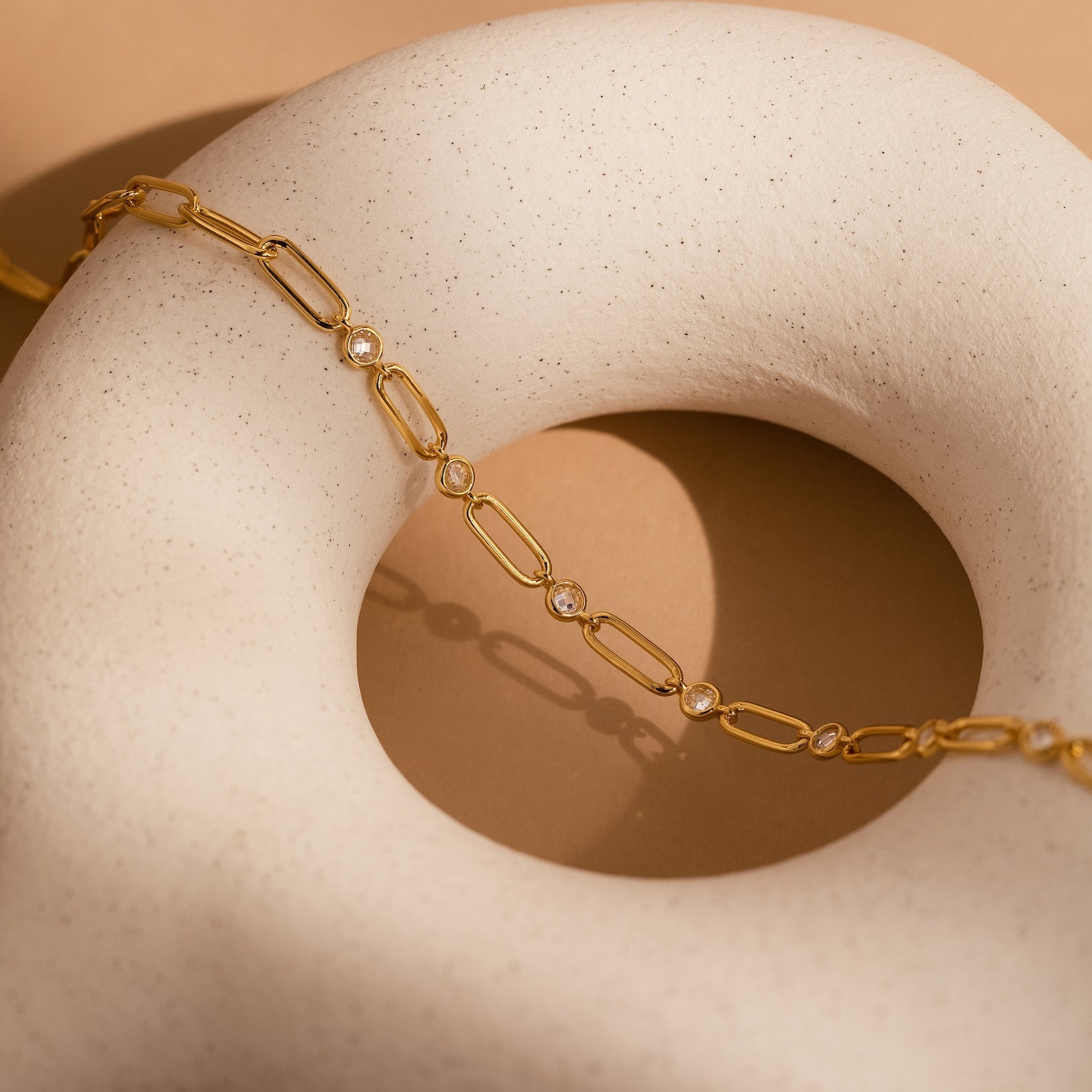 The Diamond Paperclip Necklace, adorned with clear gemstones, drapes elegantly over a smooth white, donut-shaped sculpture, showcasing the refined allure of statement jewelry.