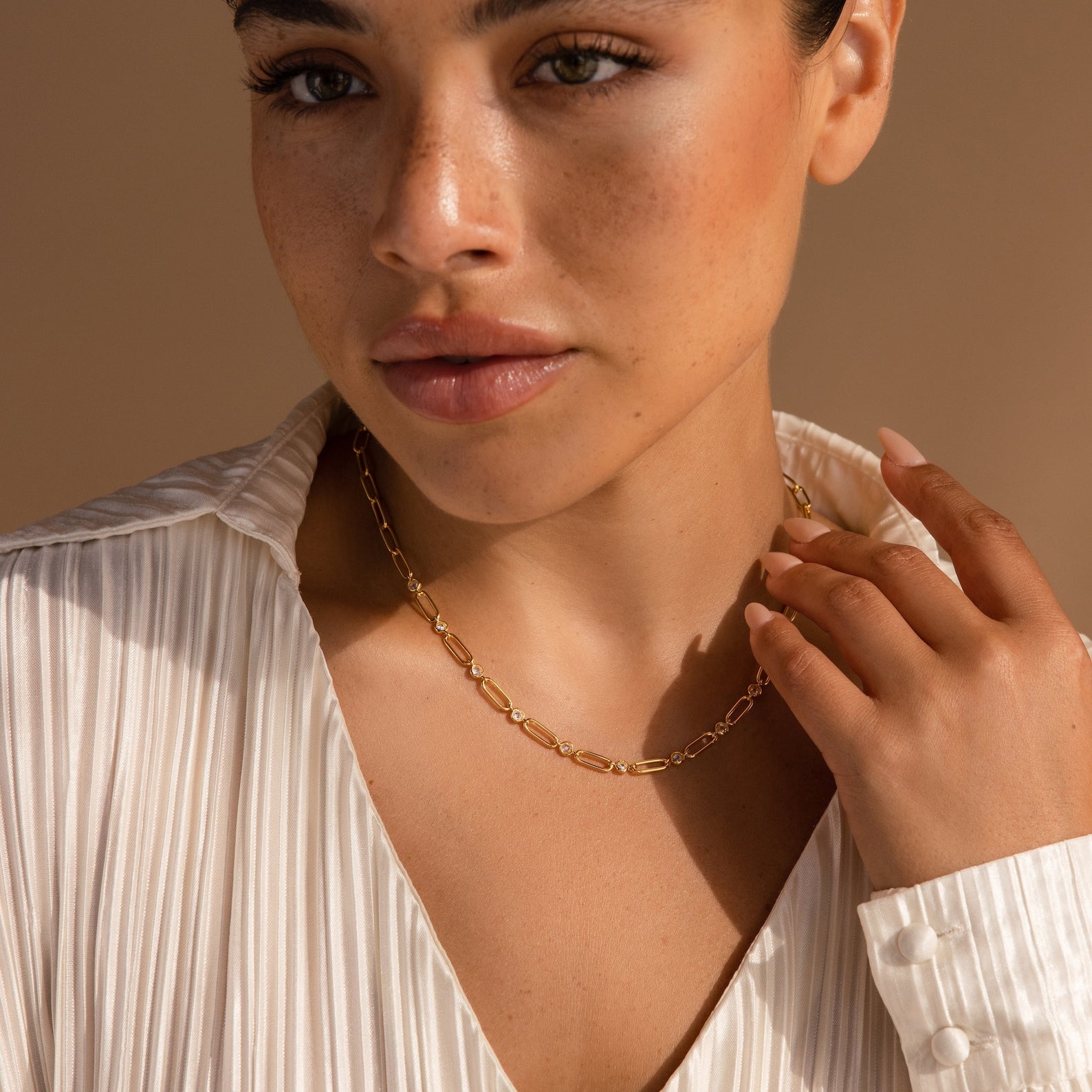 A woman in a cream pleated blouse touches her Diamond Paperclip Necklace, showcasing the statement jewelry.