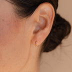 Close-up of a woman's ear wearing Pink Opal Huggies—delicate gold hoop earrings featuring pink opals, ideal for fans of feminine jewelry.