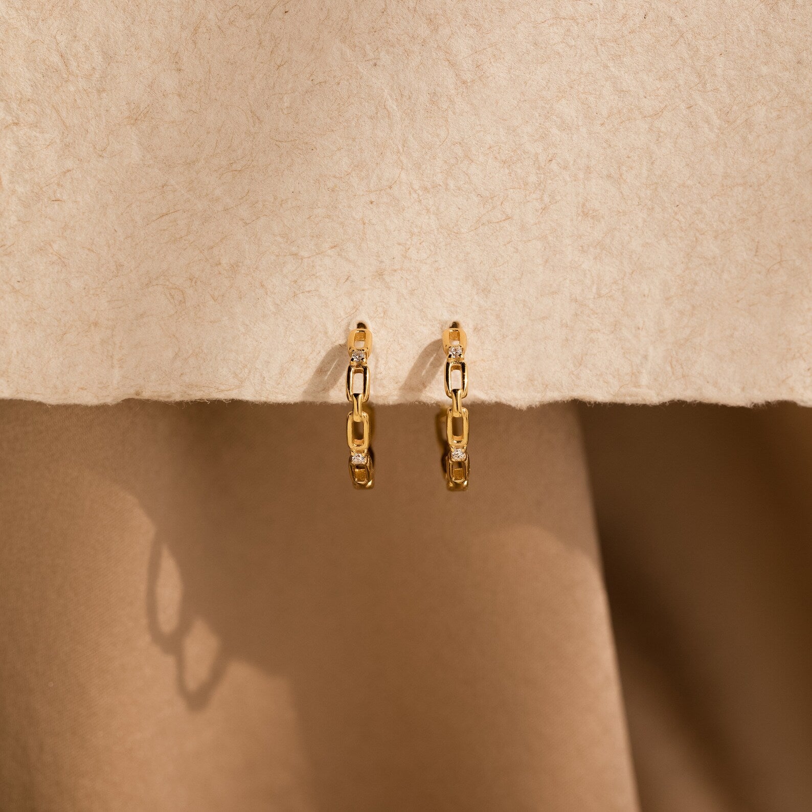 Diamond Link Hoops displayed on a textured beige surface with soft shadows—perfect as elegant wedding earrings or a chic bridal accent.