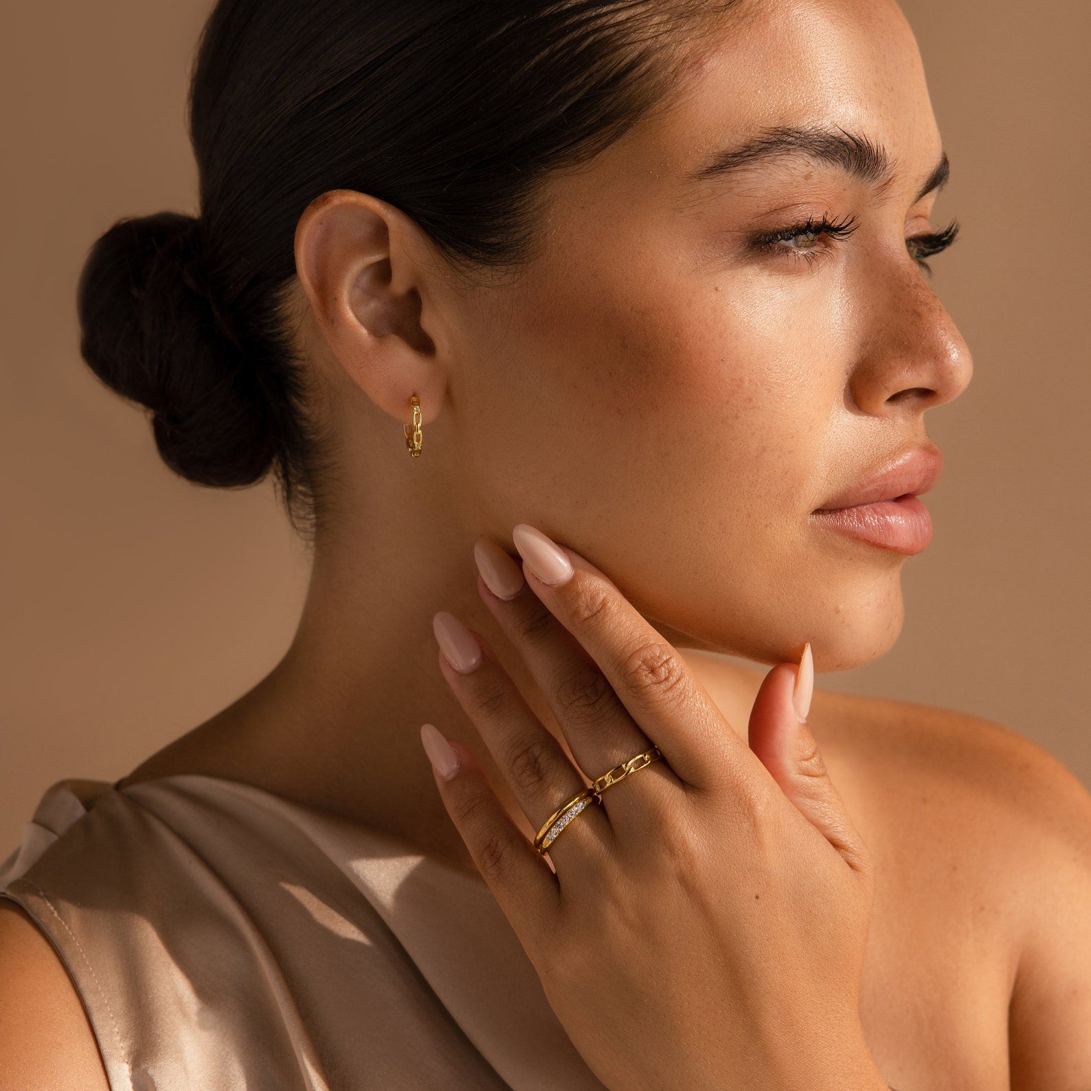 Woman with smooth skin touches her neck while wearing Diamond Link Hoops and gold rings, set against a neutral background.