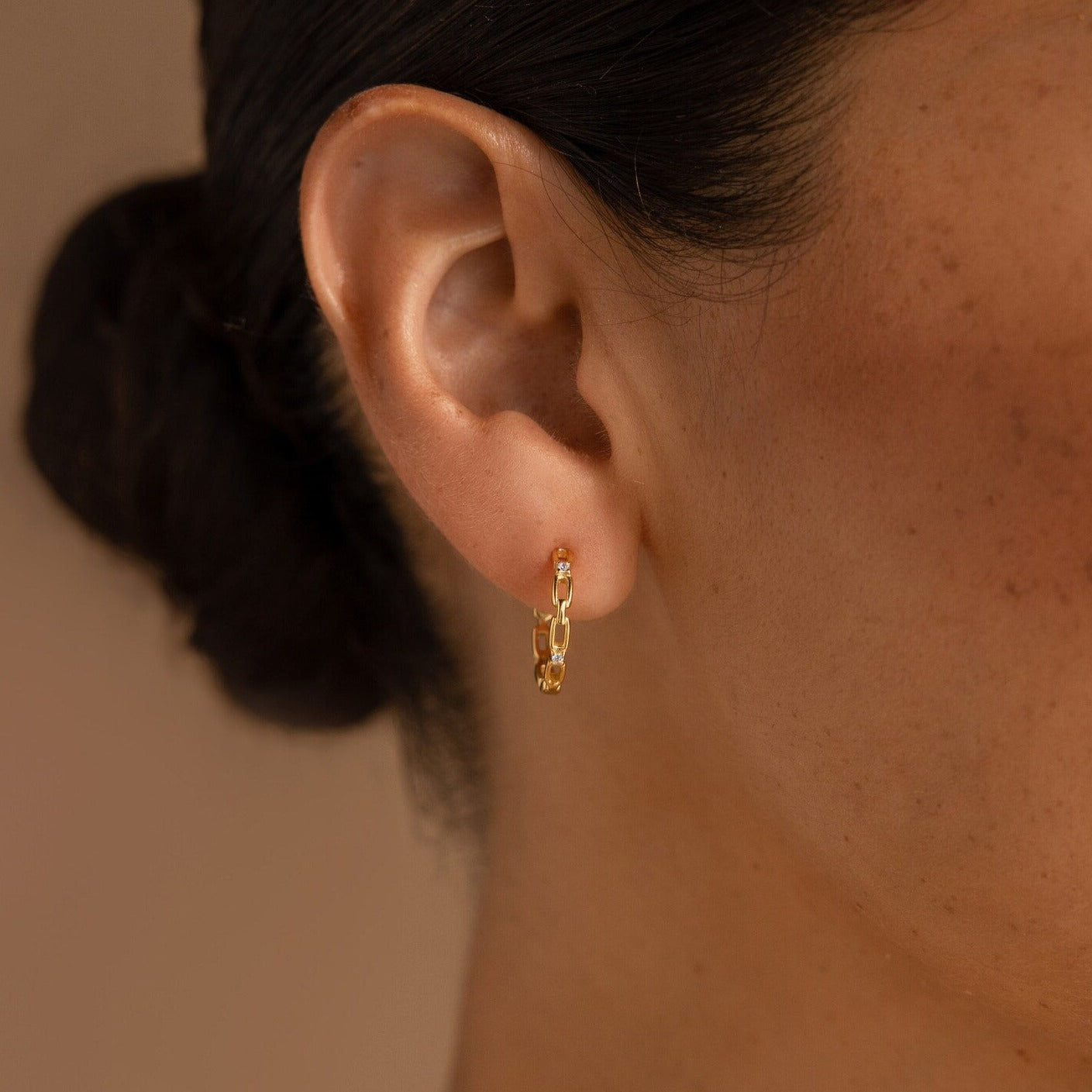 Close-up of a woman's ear wearing Diamond Link Hoops, small gold chain-link bridal earrings, with her hair pulled back.