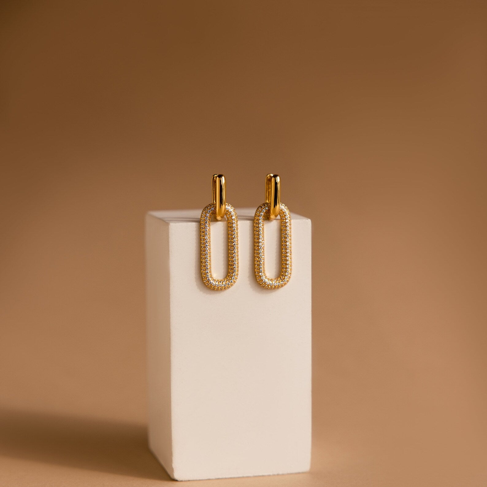 Pave Link Hoops are shown on a white rectangular stand against a brown background.