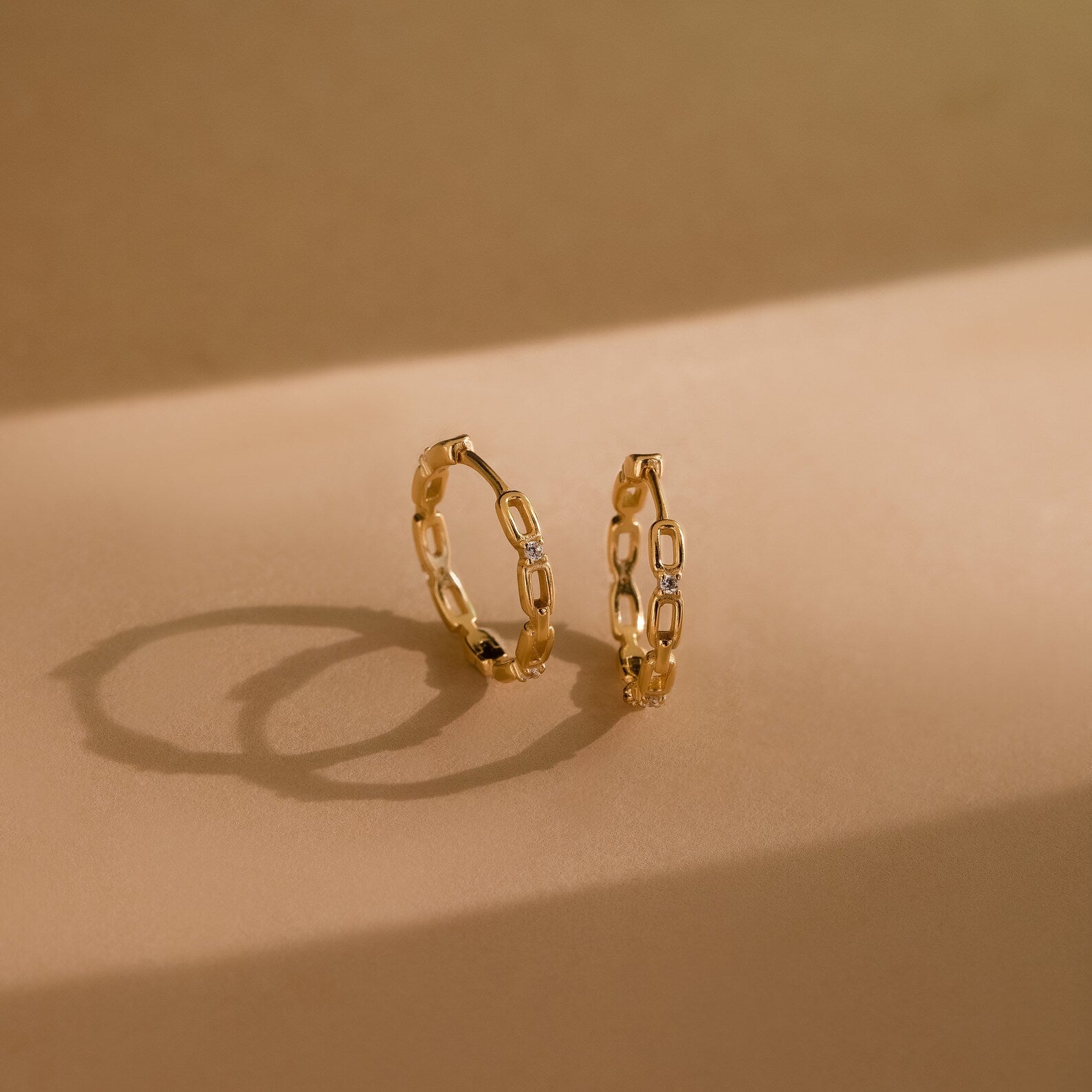 Diamond Link Hoops cast elegant shadows on a beige surface—a modern take on diamond chain link hoops, perfect as bridal or wedding earrings.