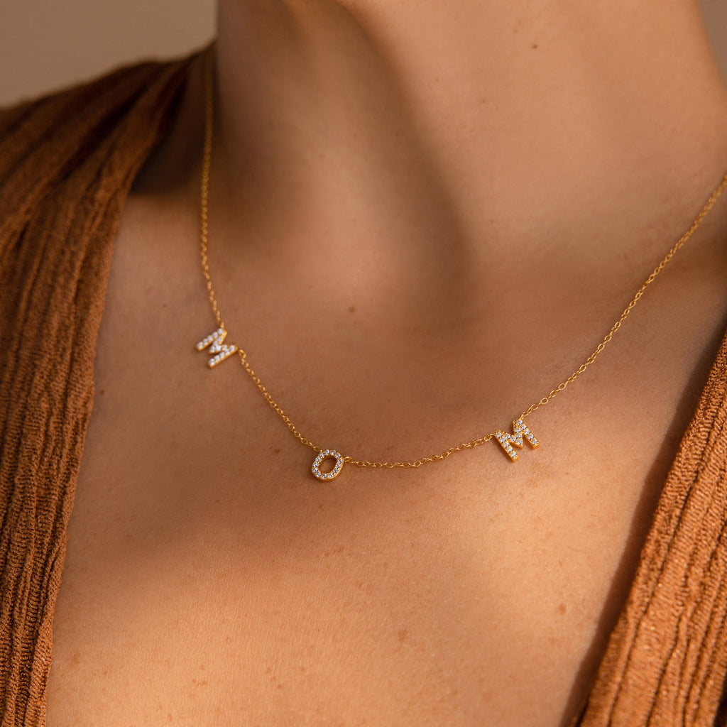 The Pave Mom Necklace, featuring sparkling diamond letters spelling "MOM," rests elegantly on the neck and makes a meaningful gift for any mother.