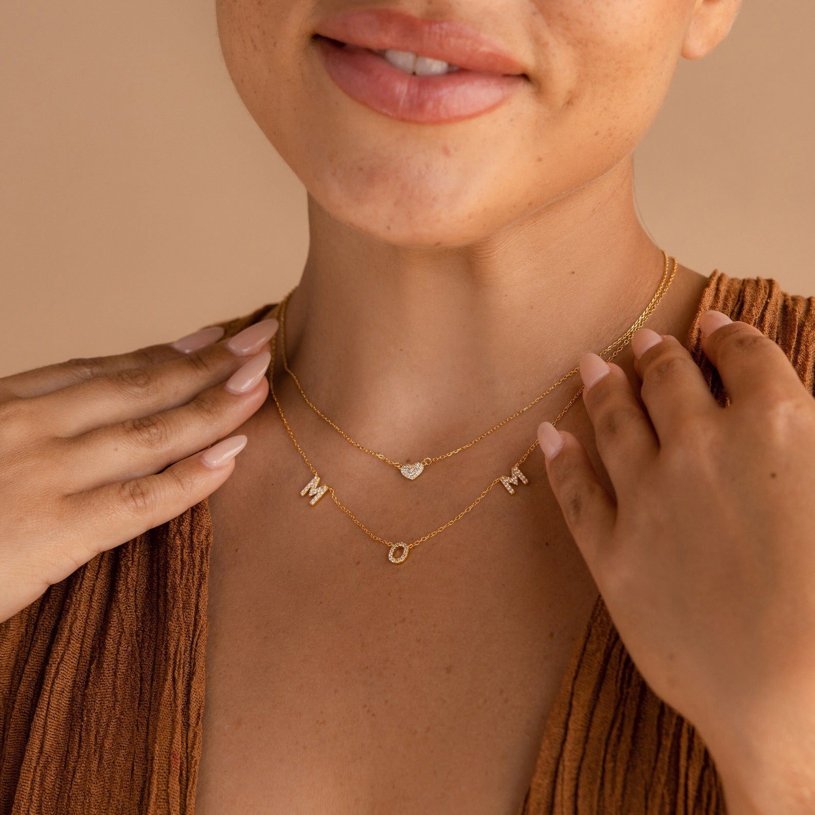 A woman wears the Pave Mom Necklace and a heart charm necklace, creating a thoughtful mom necklace duo that pairs beautifully with her brown top.