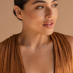 A woman wearing a brown sleeveless top and the Pave Mom Necklace, which spells “MOM” in sparkling pavé, looks off to the side—showcasing a meaningful gift perfect for any mom.