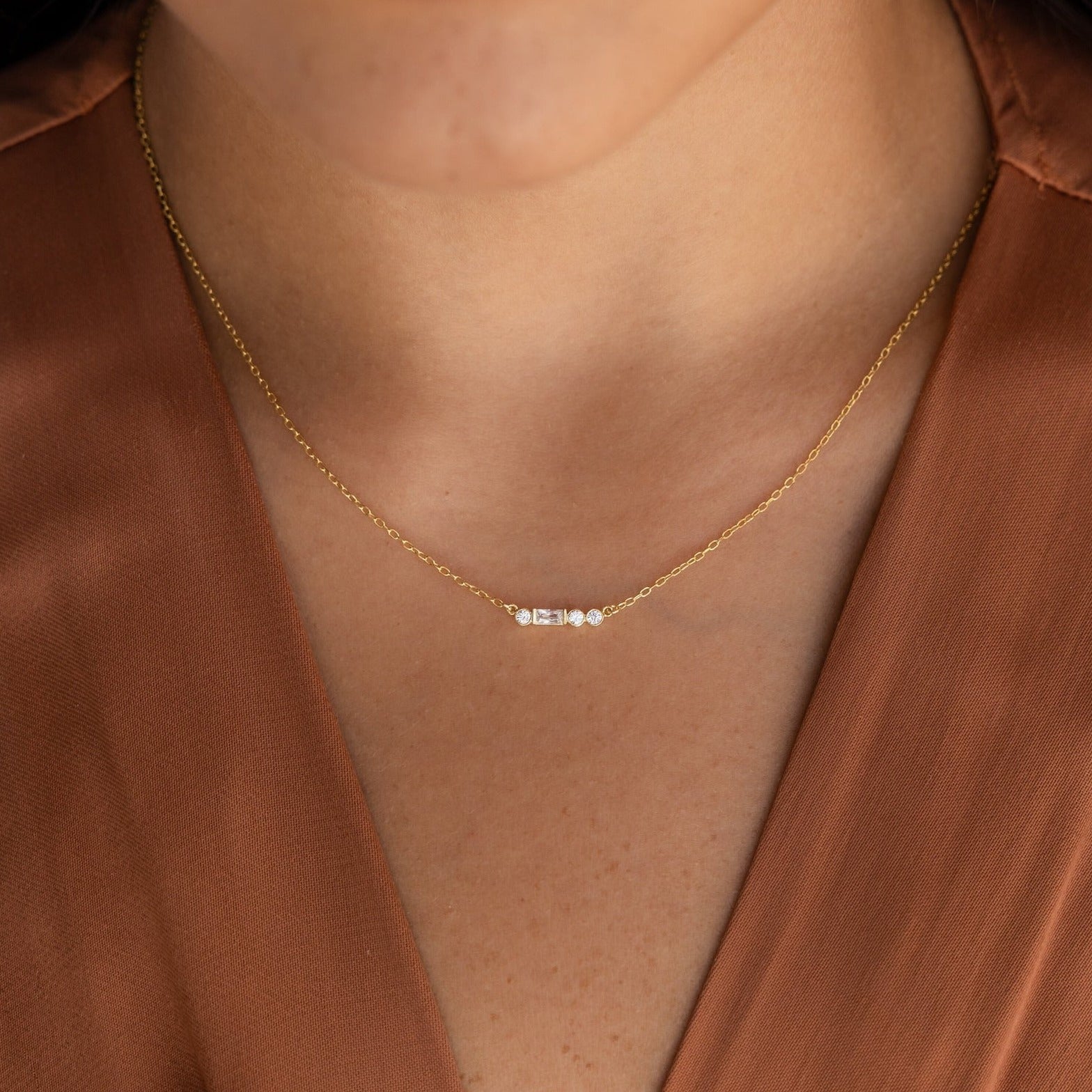 A woman wearing an Initial Morse Code Necklace with small gold beads, paired with a brown v-neck blouse.