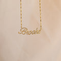 The Elegant Pave Name Necklace features "Brooke" in cursive, encrusted with sparkling gems and suspended from a chic twist chain for a personalized touch.