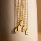 Traditional Ribbed Initial Necklaces rest on a light surface, each rectangle pendant showcasing a unique letter for a personalized charm look.