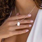 A woman with manicured nails holds the Newsletter Ribbed Initial Necklace, featuring a silver engraved pendant with the letter G.