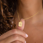 A person holds a necklace—a gold Newsletter Ribbed Initial Necklace engraved with the initial "S.