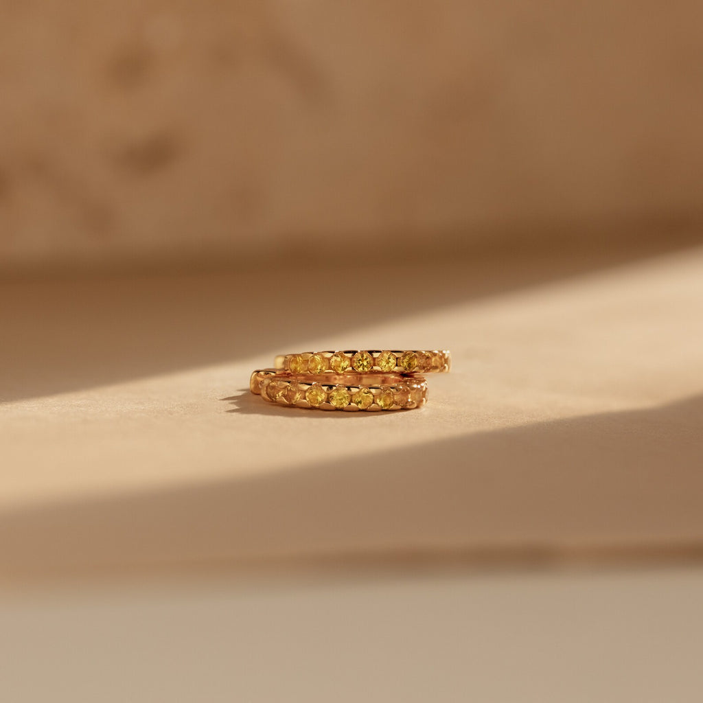 Citrine Pave Huggies featuring small yellow stones, displayed on a neutral surface under soft sunlight.