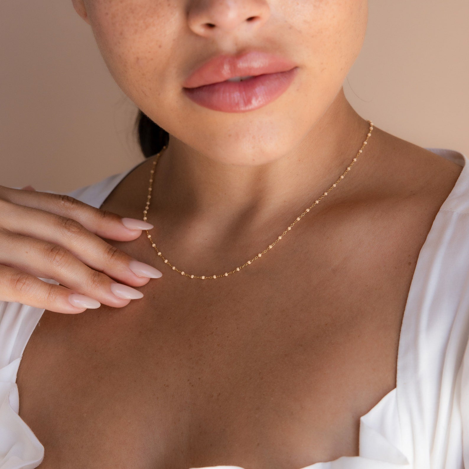 A woman showcases the Peach Station Necklace, pairing it with a white blouse and manicured nails gently resting on her collarbone for an effortlessly chic look.