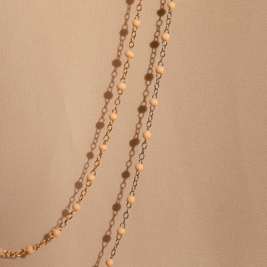 The Peach Station Necklace, featuring gold and black beads, drapes elegantly on a beige textured fabric—perfect for adding a stylish layer and elevating your beach-inspired look.