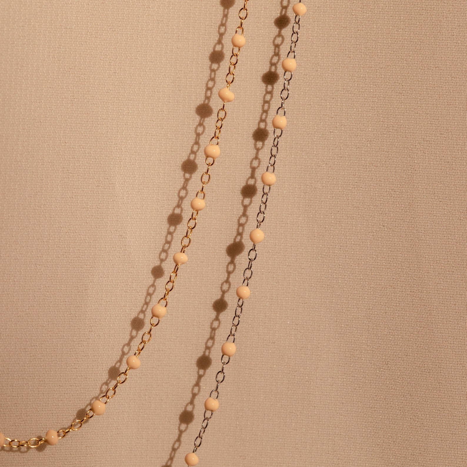 The Peach Station Necklace, featuring gold and black beads, drapes elegantly on a beige textured fabric—perfect for adding a stylish layer and elevating your beach-inspired look.