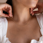 A woman in a white top wears the Peach Station Necklace, adding a subtle beach-inspired touch to her look.