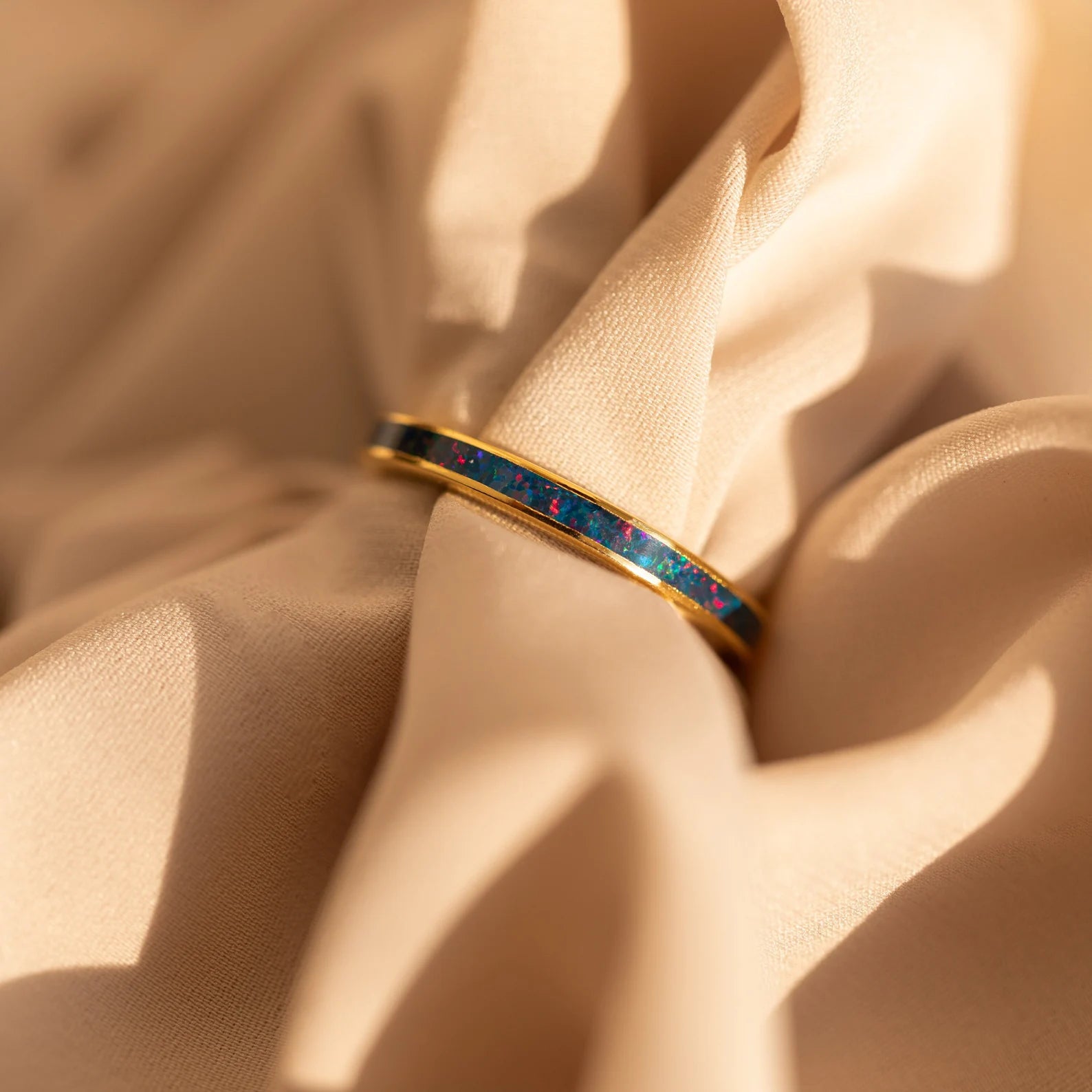 The Opal Inlay Rings Set rests on soft beige fabric, showcasing opal colors that shimmer with hints of indigo blue.