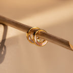 Crescent Moon Opal Huggies, featuring pink opal gemstone inlay, hang on a thin diagonal bamboo stick set against a beige background.