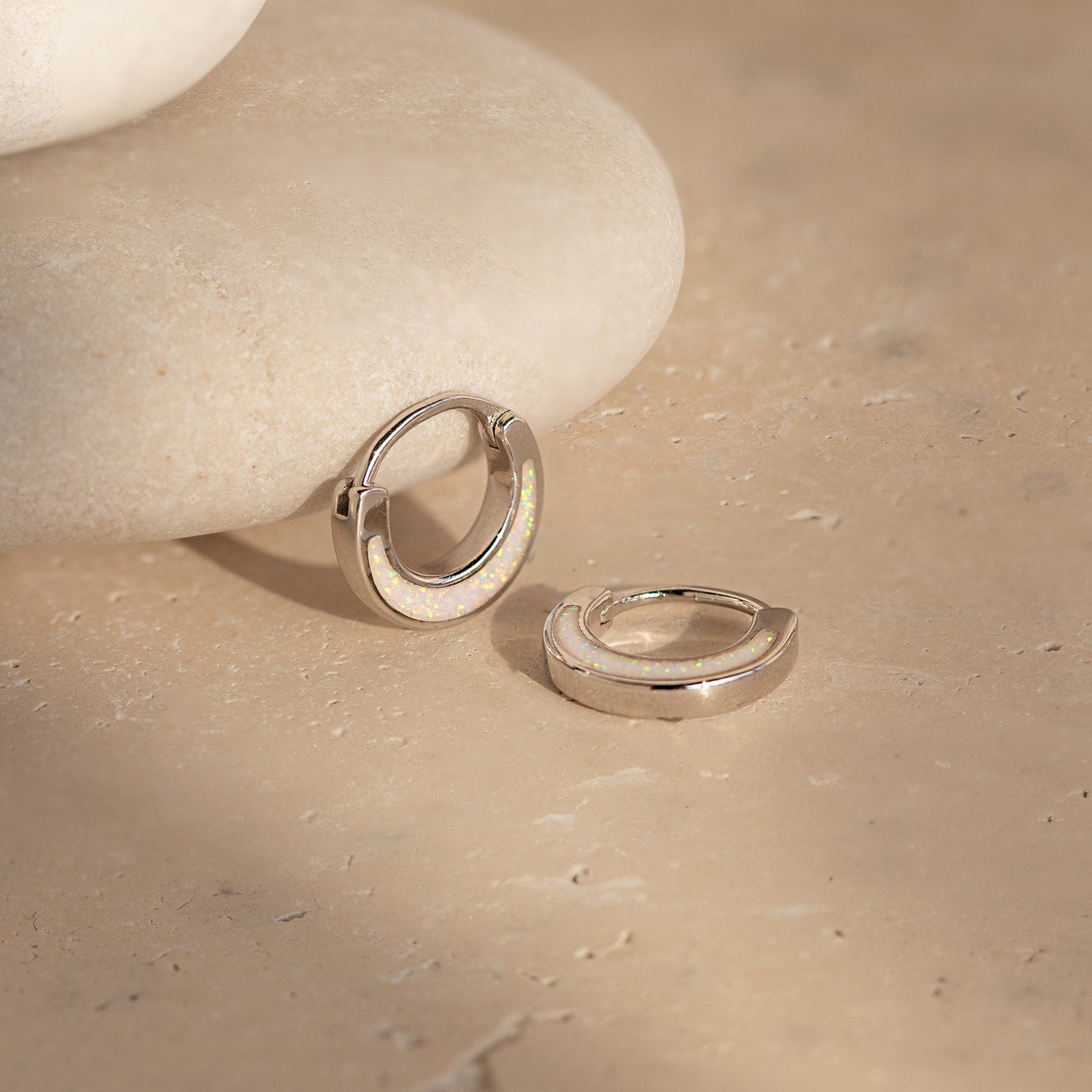 Crescent Moon Opal Huggies elegantly displayed on a rock, these huggie hoop earrings highlight the captivating beauty of opal gemstones.