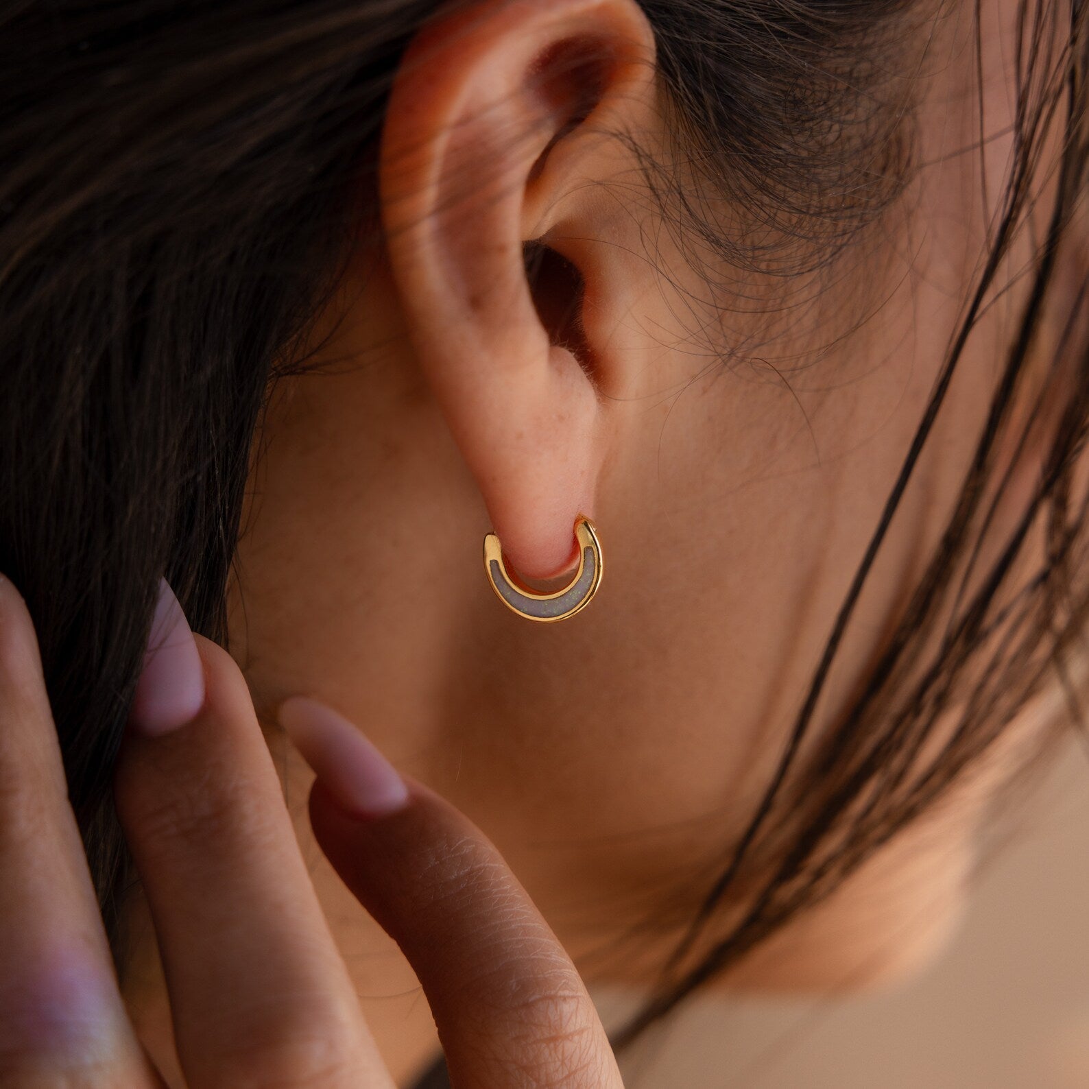 A close-up of a woman's ear adorned with Crescent Moon Opal Huggies, showcasing the luminous beauty of the opal gemstone.