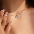A close-up of a woman wearing the Elegant Pave Name Necklace on a twist chain, her manicured fingers gently touching her collarbone for a chic, personalized accessory look.