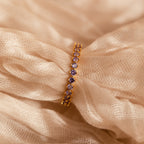 The Amethyst Eternity Ring, featuring minimalist purple amethysts, rests on soft, textured beige fabric. This elegant ring is perfect for any occasion.