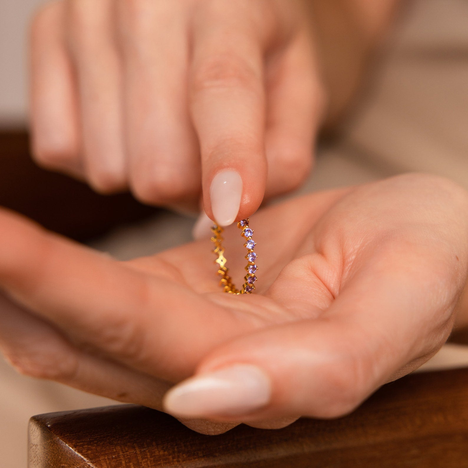 A person holds the Amethyst Eternity Ring, a delicate minimalist band adorned with small purple amethyst gemstones, between their fingers.