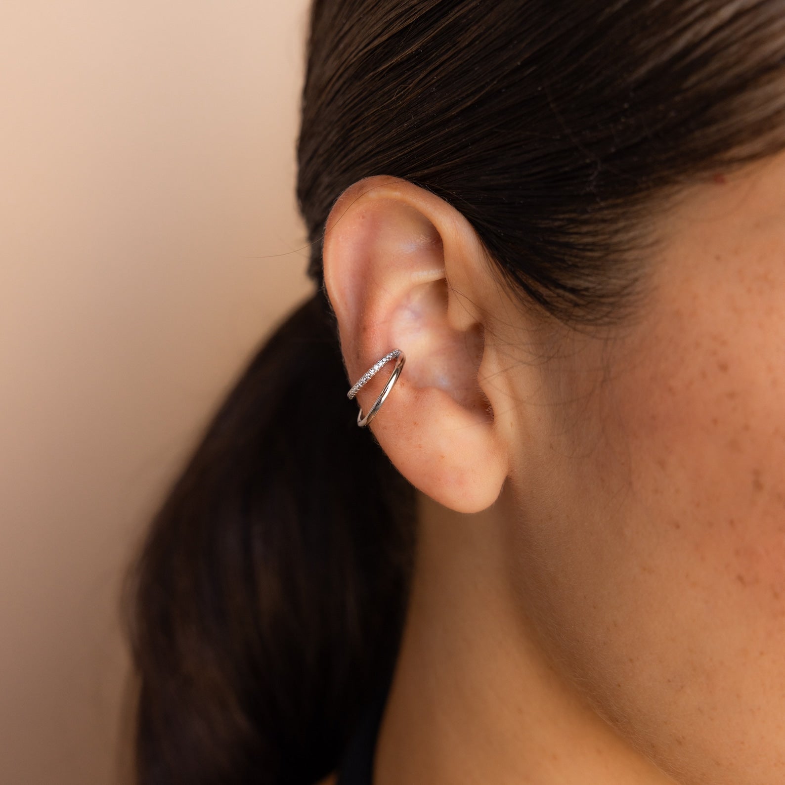 Close-up of a person’s ear styled with Lydia Duo Cuffs, featuring multilayered silver hoops; hair is tied back in a low ponytail.