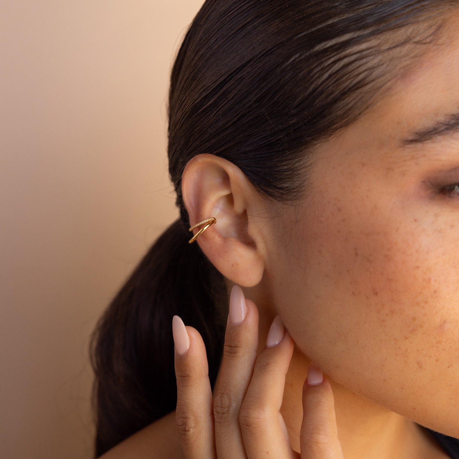 A woman with dark hair wears Lydia Duo Cuffs and touches her ear with manicured fingers.