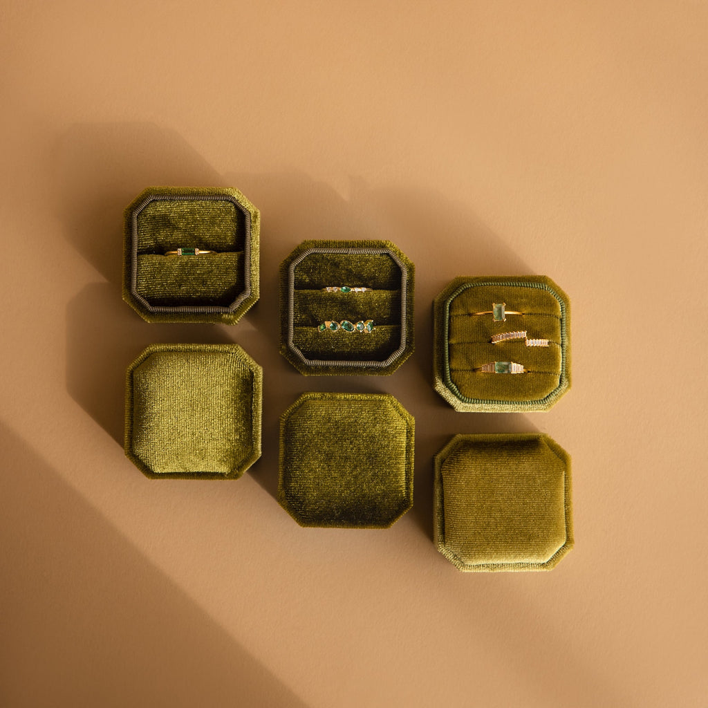 Six green Velvet Ring Boxes, including standard and 3-slot designs, are arranged on a tan surface—some open to display rings and earrings.