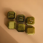Six green Velvet Ring Boxes, including standard and 3-slot designs, are arranged on a tan surface—some open to display rings and earrings.