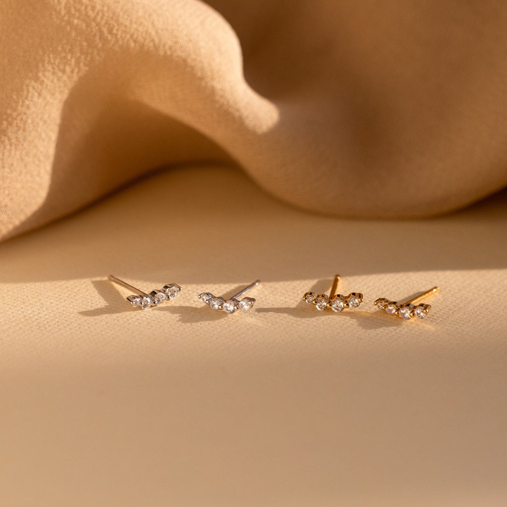 Two pairs of elegant Tiny Diamond Climbers earrings—one in silver and one in gold—feature delicate crystals on a beige fabric background, making them a perfect anniversary gift.